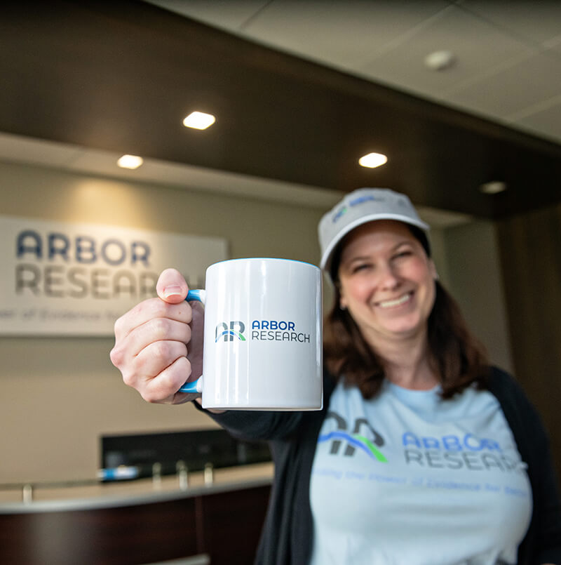 Smiling employee proudly holds an Arbor Research branded coffee mug